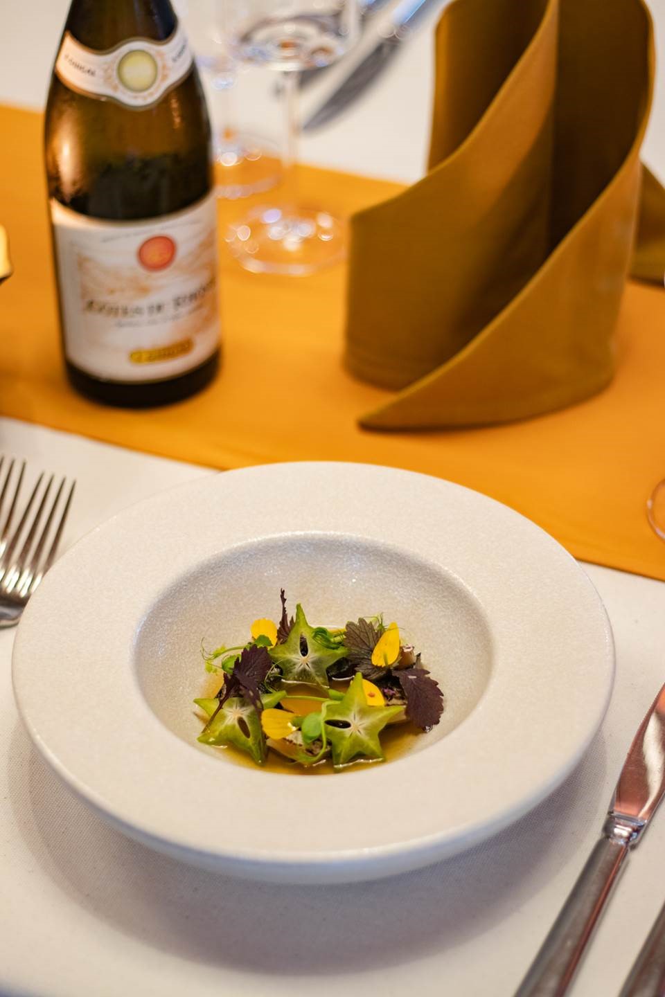 An entrée of salted mackerel with fermented star fruit, sour broth, chrysanthemum, and coriander oil.