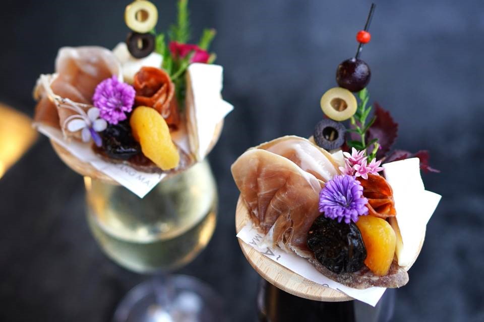“Charcuterie Wine Glass Toppers” are served on Wednesdays from 6pm-midnight. A glass of red or white wine is artfully topped with a charcuterie set.